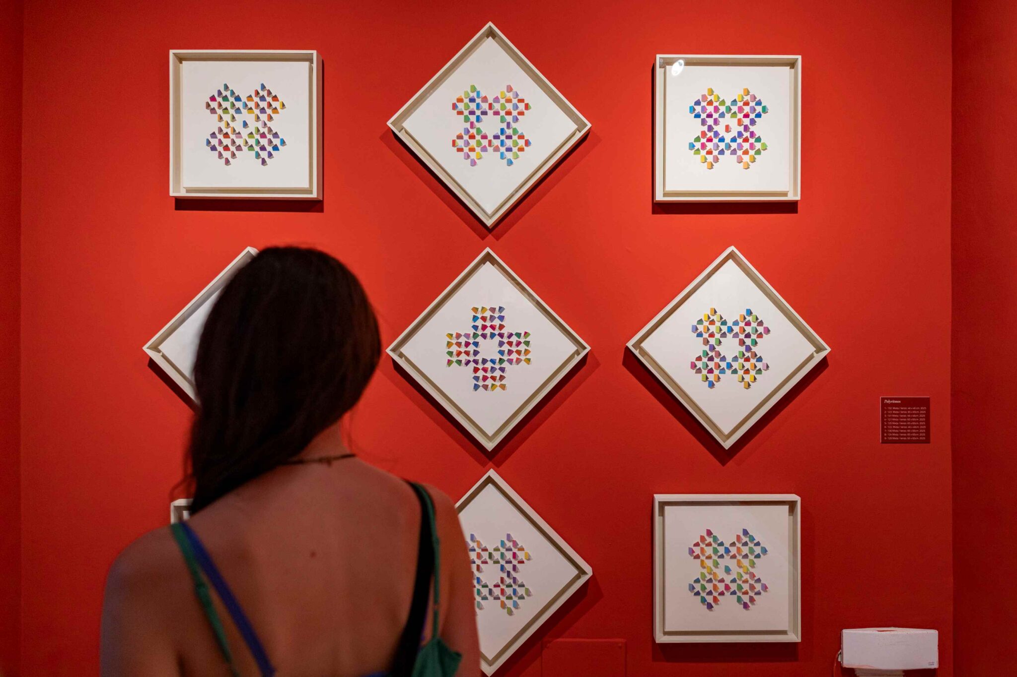 Gallery wall with diamond-framed mosaic artworks made of multicolored triangles; person viewing from foreground.